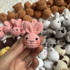 A hand holds a small pink crocheted rabbit, surrounded by various handcrafted crochet animals.