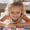 A young girl is playing with a pink portable folding magnetic puzzle set on a white surface.