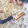 Hands are assembling an urban oil painting jigsaw puzzle for adults and families on a table.