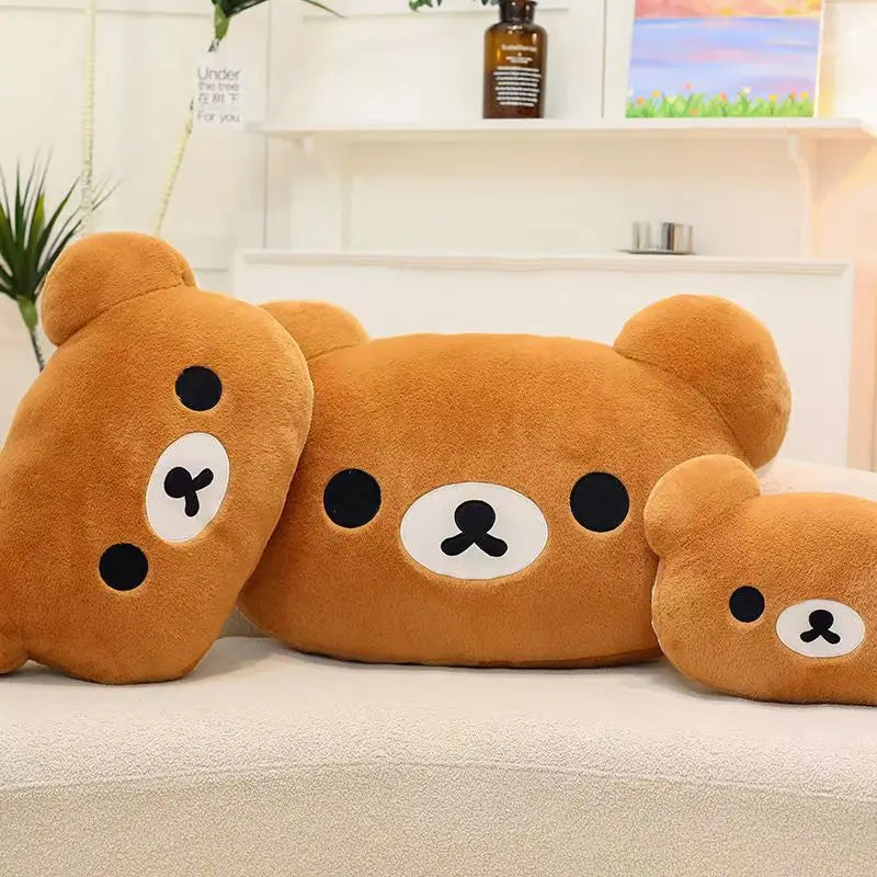 Three soft brown Rilakkuma plush hand rest pillows resting on a white surface.
