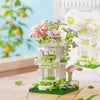 A mini building set featuring a pink and green woodland cabin and windmill structure with floral accents.