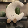 A white crescent moon plushie with a smiling face is displayed next to two green cactus-shaped objects.