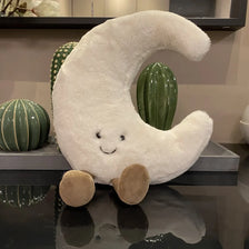 A white crescent moon plushie with a smiling face is displayed next to two green cactus-shaped objects.