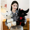 A woman holds a black Toothless dragon plush toy with red accents and a white stuffed animal in a gray sweater.