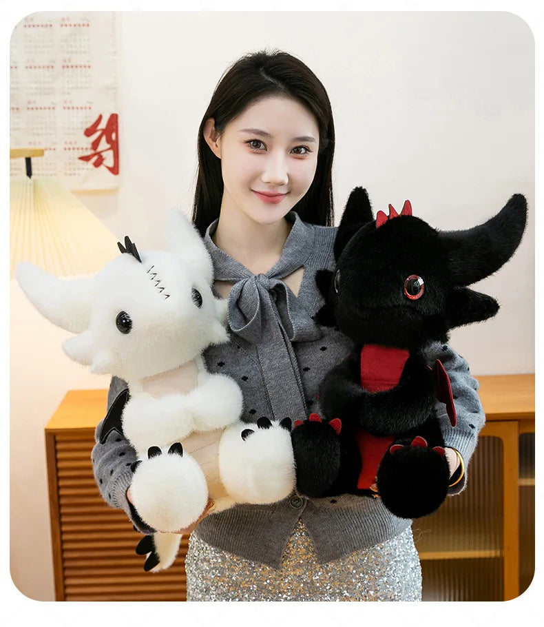 A woman holds a black Toothless dragon plush toy with red accents and a white stuffed animal in a gray sweater.