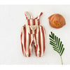 A striped baby romper in terracotta and cream with a bear decoration, next to an orange hat and a green leaf.