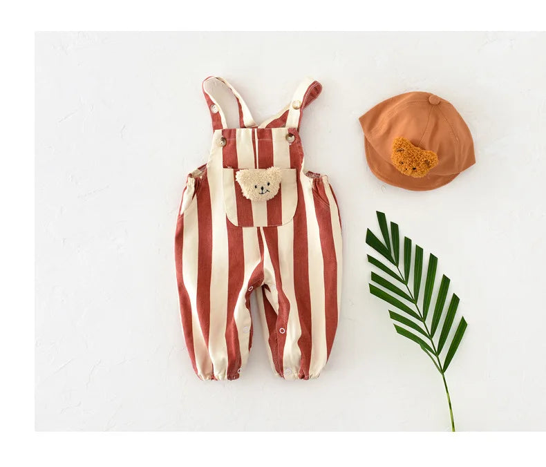 A striped baby romper in terracotta and cream with a bear decoration, next to an orange hat and a green leaf.