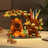 An orange Capybara building block pen holder and desk organizer featuring a wooden animal figure and various pens and plant e