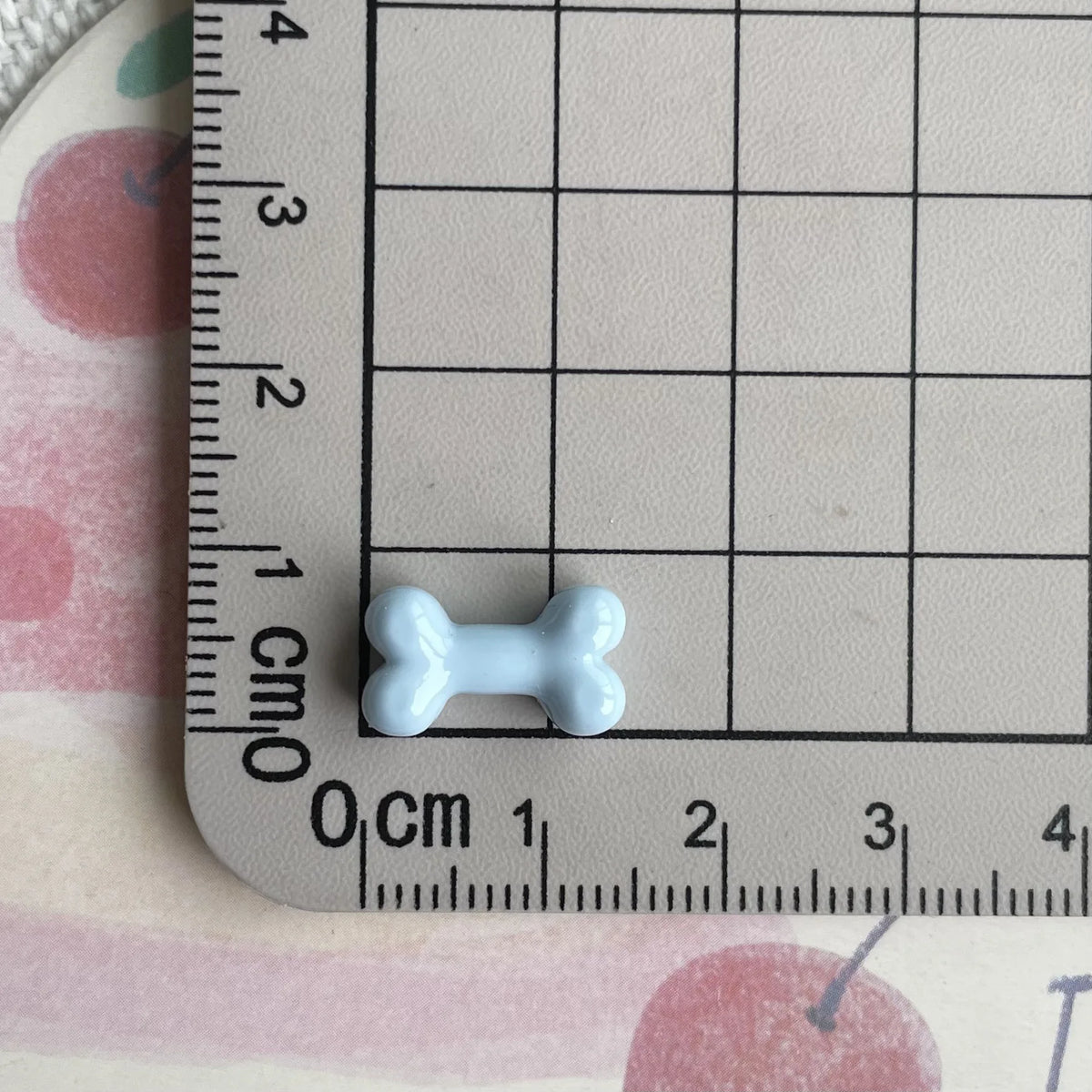 A small white resin bone charm is placed on a ruler marked in centimeters and inches.