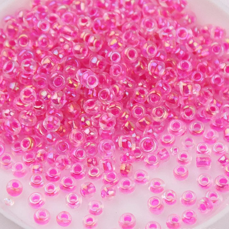 A pile of small, round pink and clear glass rice beads for DIY jewelry and crafting.