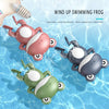 Three wind-up swimming frog toys in pink, gray, and green floating in clear water.