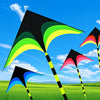 A large delta kite with a black and green canopy is flying against a bright blue sky over green fields.