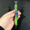 A hand holds a colorful diamond painting pen with a stainless steel tip, displaying various shades of green and blue.