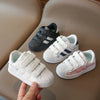 A hand holds a pair of white and navy kids' breathable casual sneakers with hook-and-loop closure.