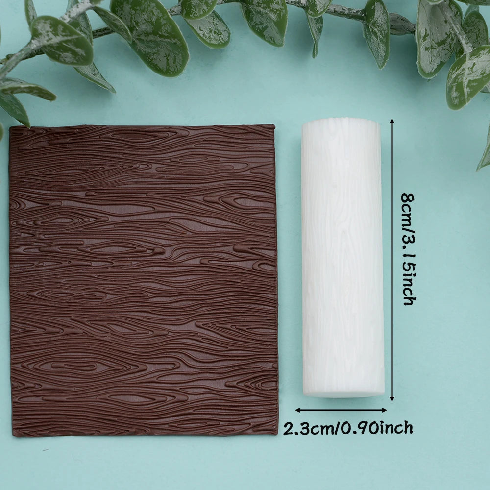 A roll of white floral texture roller for polymer clay and crafting placed on a light blue surface with green leaves.