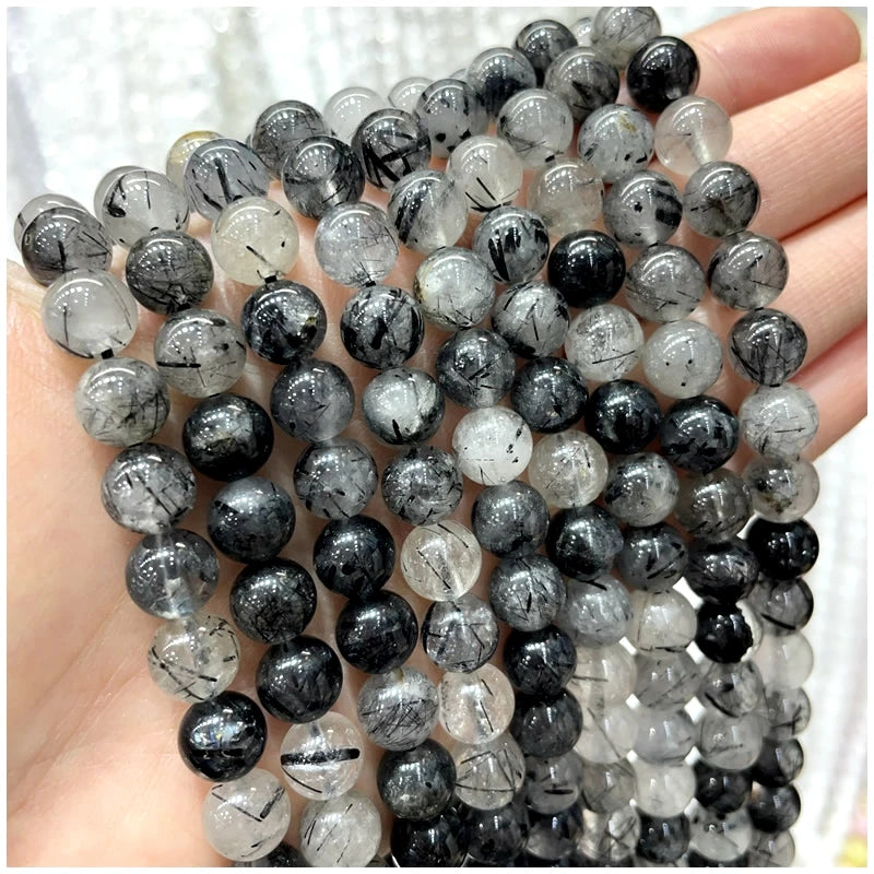 A hand holds a strand of natural stone beads including amethyst, garnet, and labradorite for DIY jewelry making.