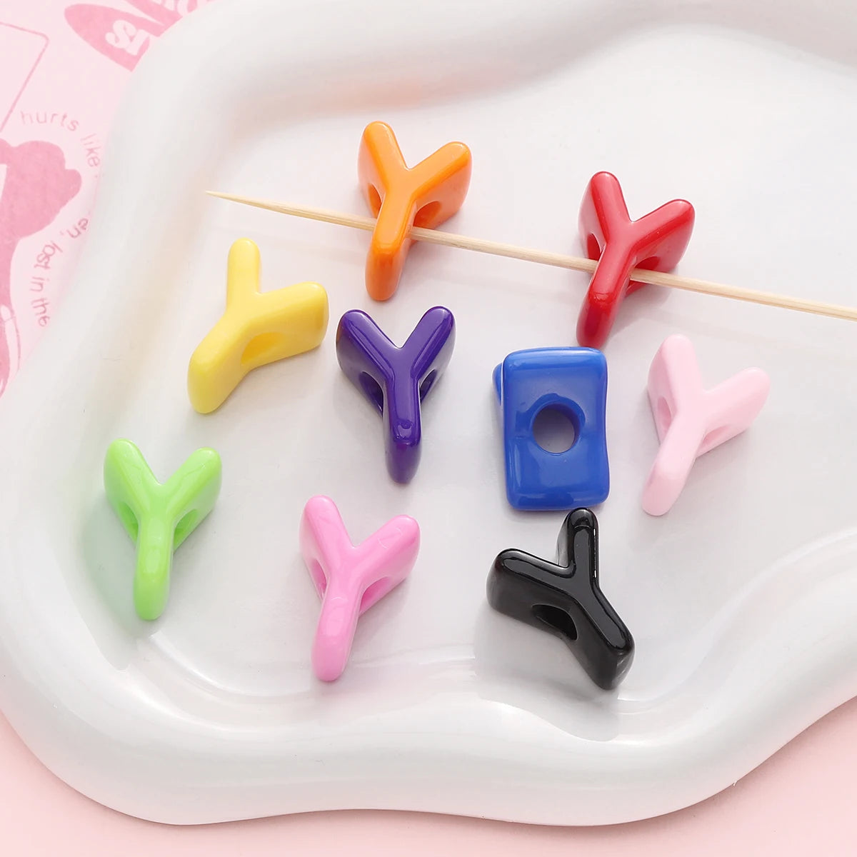A collection of colorful acrylic letter beads in various shapes and colors arranged on a white plate.