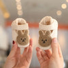 A pair of adorable bear soft sole first walker shoes for babies being held by a person.