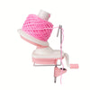 A pink hand crank yarn winder device with a pink ball of yarn and a metal frame.