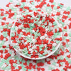 A white bowl filled with red and green cartoon polymer clay slices for slime and craft projects scattered on a white surface.
