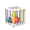 A white Montessori shape sorter cube with colorful fabric strings inside.