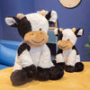 A white and black cow plush toy with brown accents sitting on a wooden surface.
