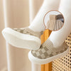 A pair of beige and white plaid slip-on toddler shoes for first walkers shown on a person's foot.