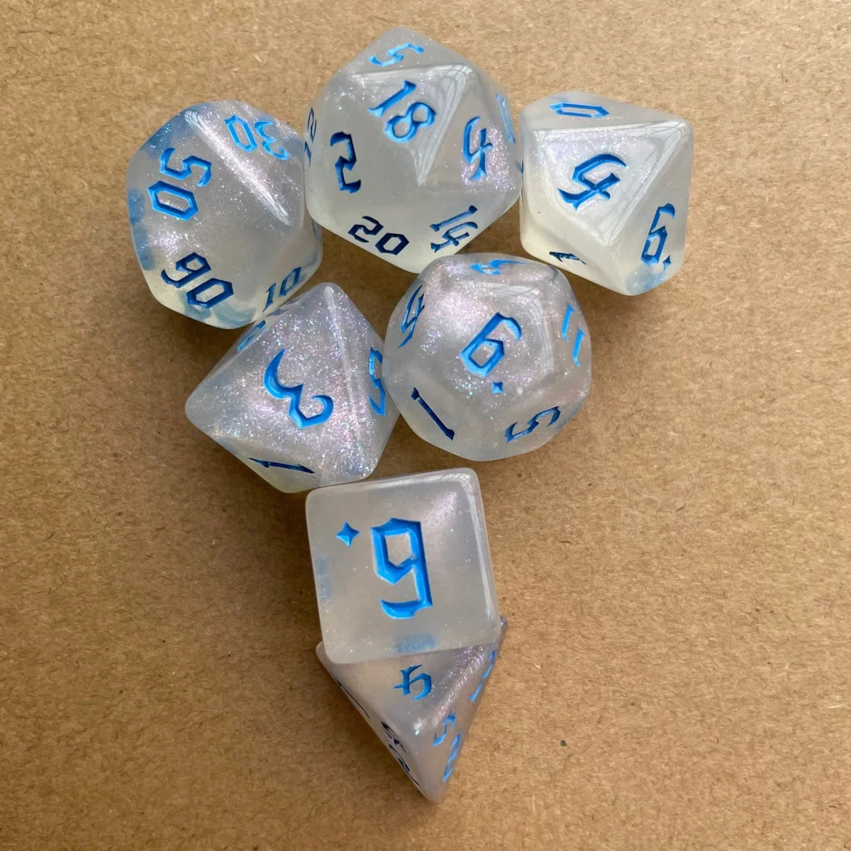 A collection of seven glitter gold polyhedral dice showing various numbers and symbols on a brown surface.