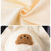 A close-up of a cream colored cotton muslin baby romper and hat set.