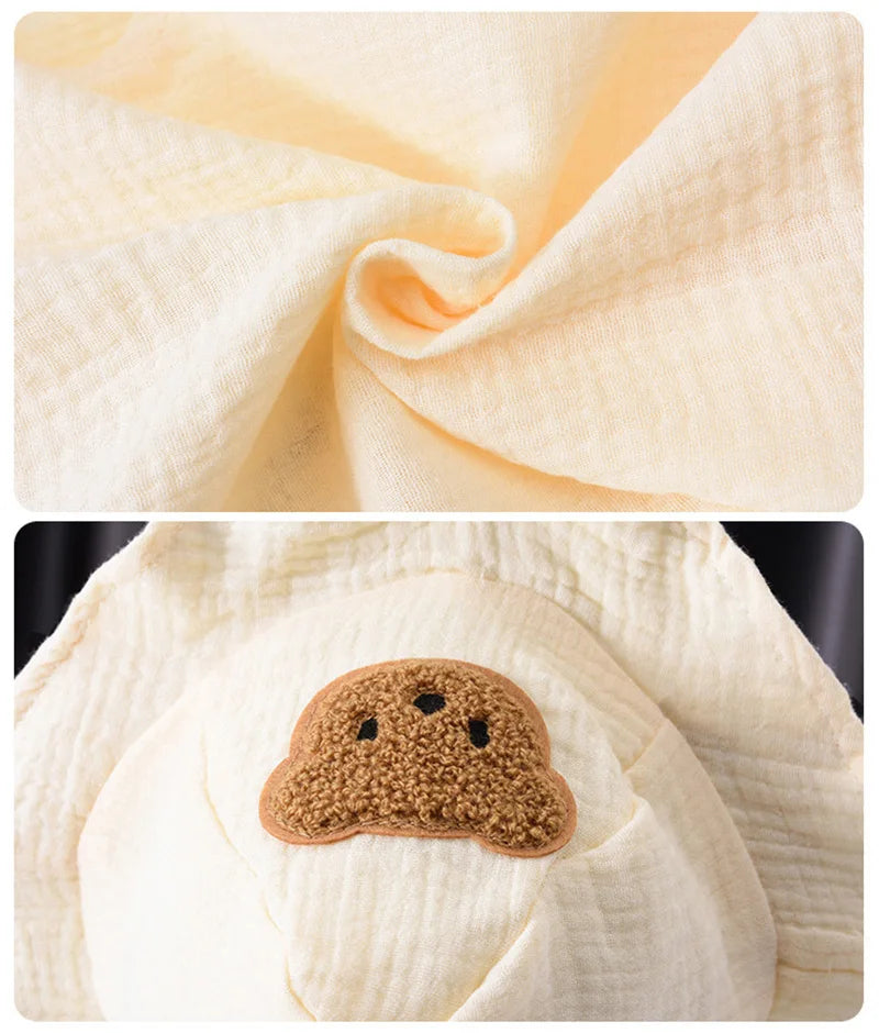 A close-up of a cream colored cotton muslin baby romper and hat set.