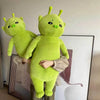 A bright lime green alien cat plush toy with large eyes and antennae standing next to a piece of art.