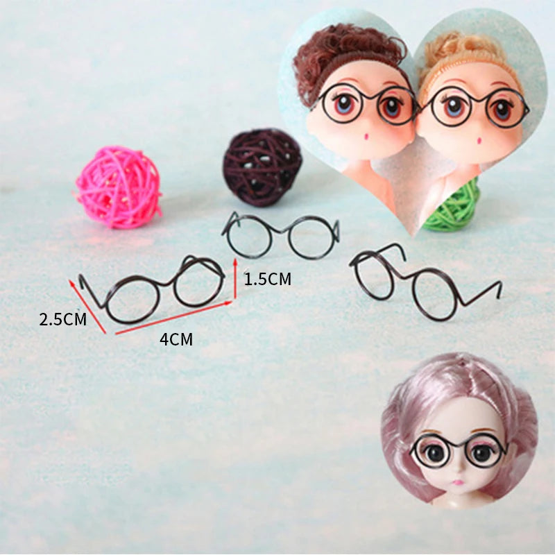 A collection of five metal round glasses frames, including a pair on a doll's face and several separate frames.