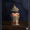 A collectible figurine of a small, frowning character dressed in dark blue and gray, standing in a stone tower setting.
