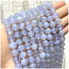 A hand holds a strand of round, translucent purple and blue natural stone beads for jewelry making.