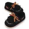 A pair of black baby first walker sneakers with brown ribbon ties and white stitching.