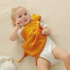 A baby is holding an orange soft cotton muslin blanket while lying on a light textured surface.