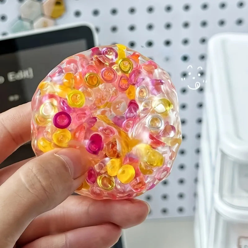 A hand holds a translucent, colorful fidget ball made of soft silicone, featuring pink, yellow, and purple hues.