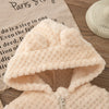 A light pink plush hooded winter jacket for a baby girl displayed on a wooden surface.