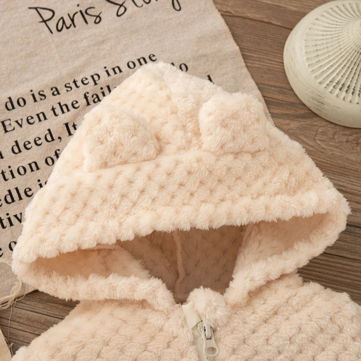 A light pink plush hooded winter jacket for a baby girl displayed on a wooden surface.