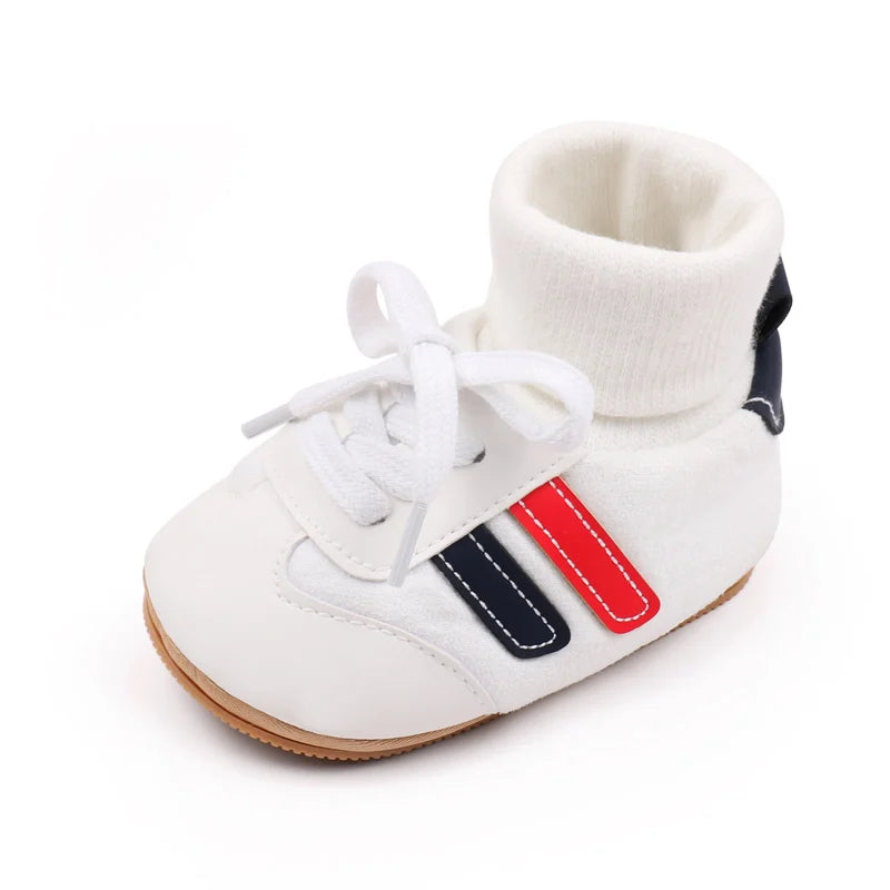 White baby booties with a knitted cuff and anti-slip sole featuring black and red accents.