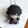 A black anime character plushie pendant charm with large purple eyes and dark hair resting on a piece of paper.