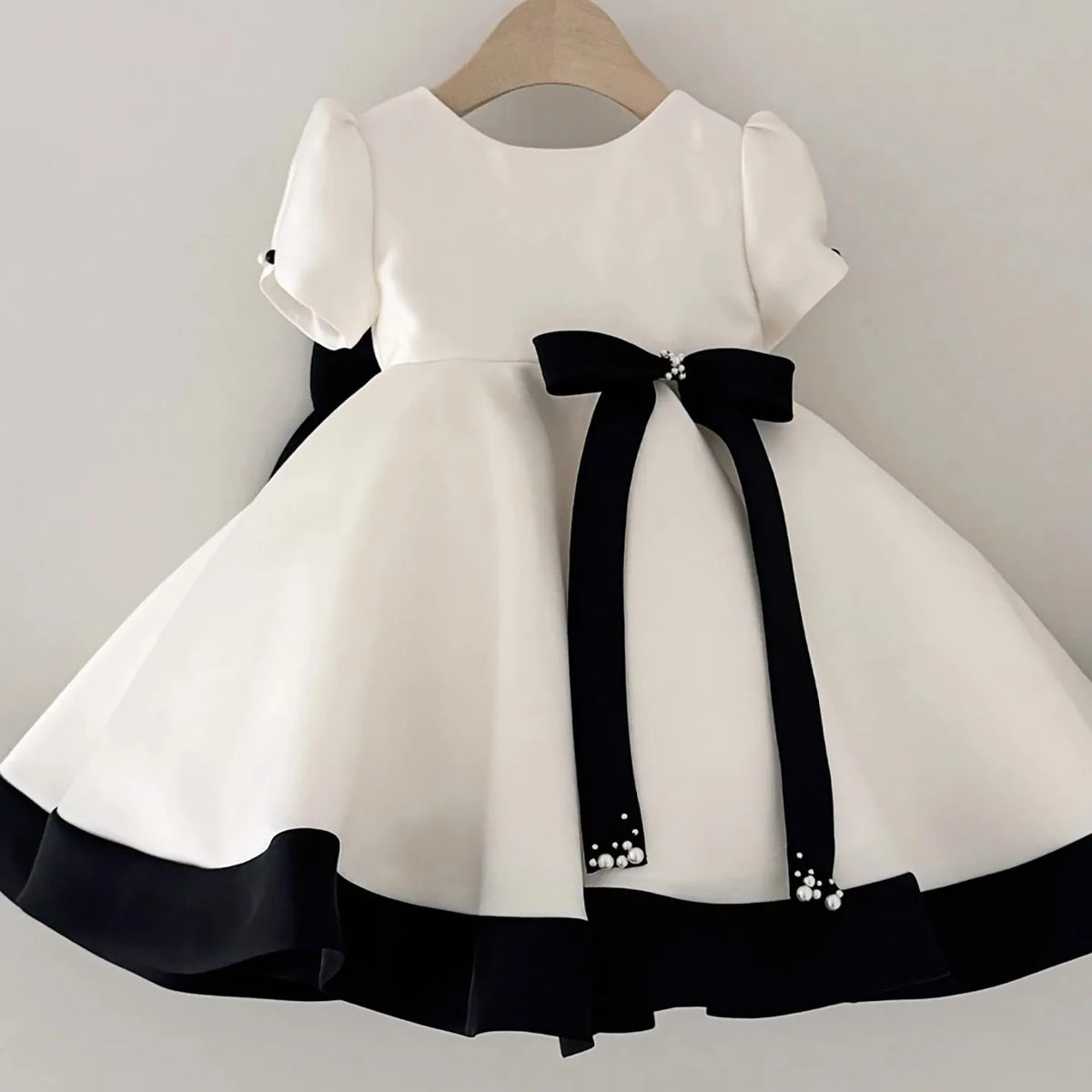 White princess tulle dress with black ribbon details displayed on a hanger.