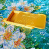 A yellow diamond painting organizer tray with storage compartments is shown on a colorful fabric background.