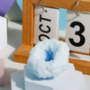 A light blue squishy stress relief ball is displayed on a white block in front of a wooden frame with numbered cards.
