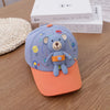 A light blue toddler baseball cap featuring a cute gray bear design and an orange brim, resting on a wooden surface.