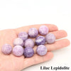 A hand holds several lilac lepidolite crystal spheres of varying sizes and shades.