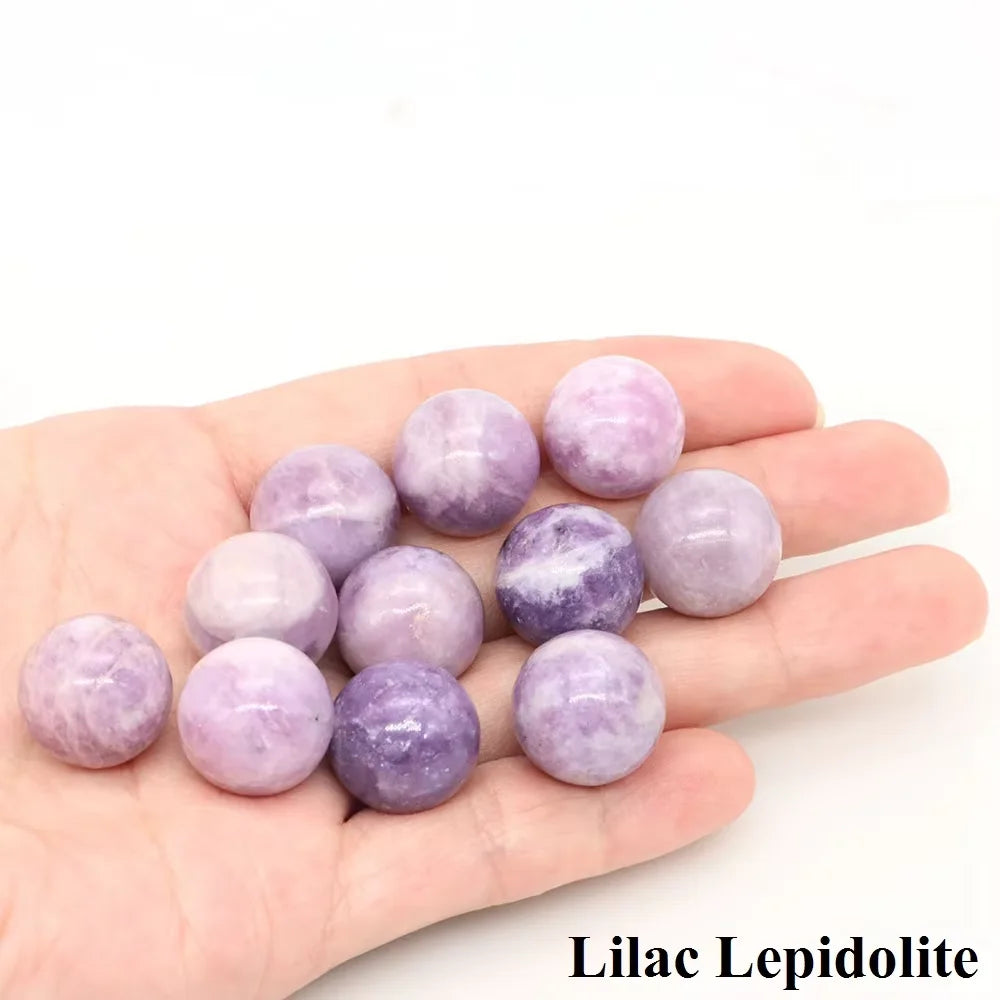 A hand holds several lilac lepidolite crystal spheres of varying sizes and shades.