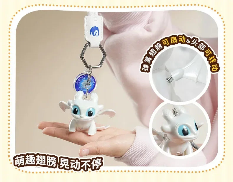 A white Toothless dragon keychain with movable wings and glowing eyes is displayed on a person's hand.