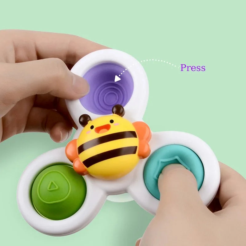 A hand is pressing a yellow bee bath toy with suction cups onto a white ring, demonstrating its use.