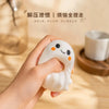 A hand holds a white, squishy ghost-shaped stress ball with black eyes and orange accents.
